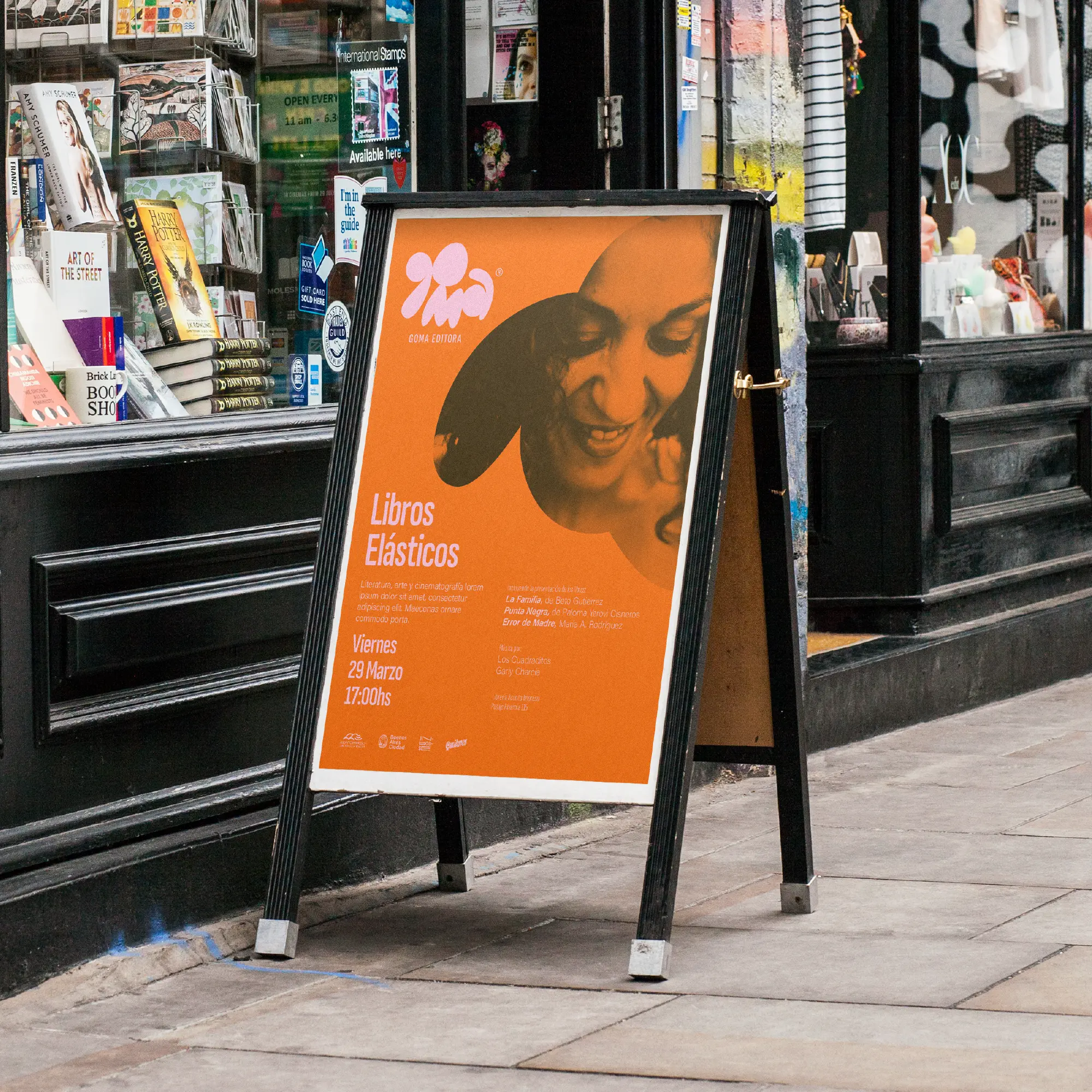 Orange Goma event poster displayed on a sidewalk sign.
